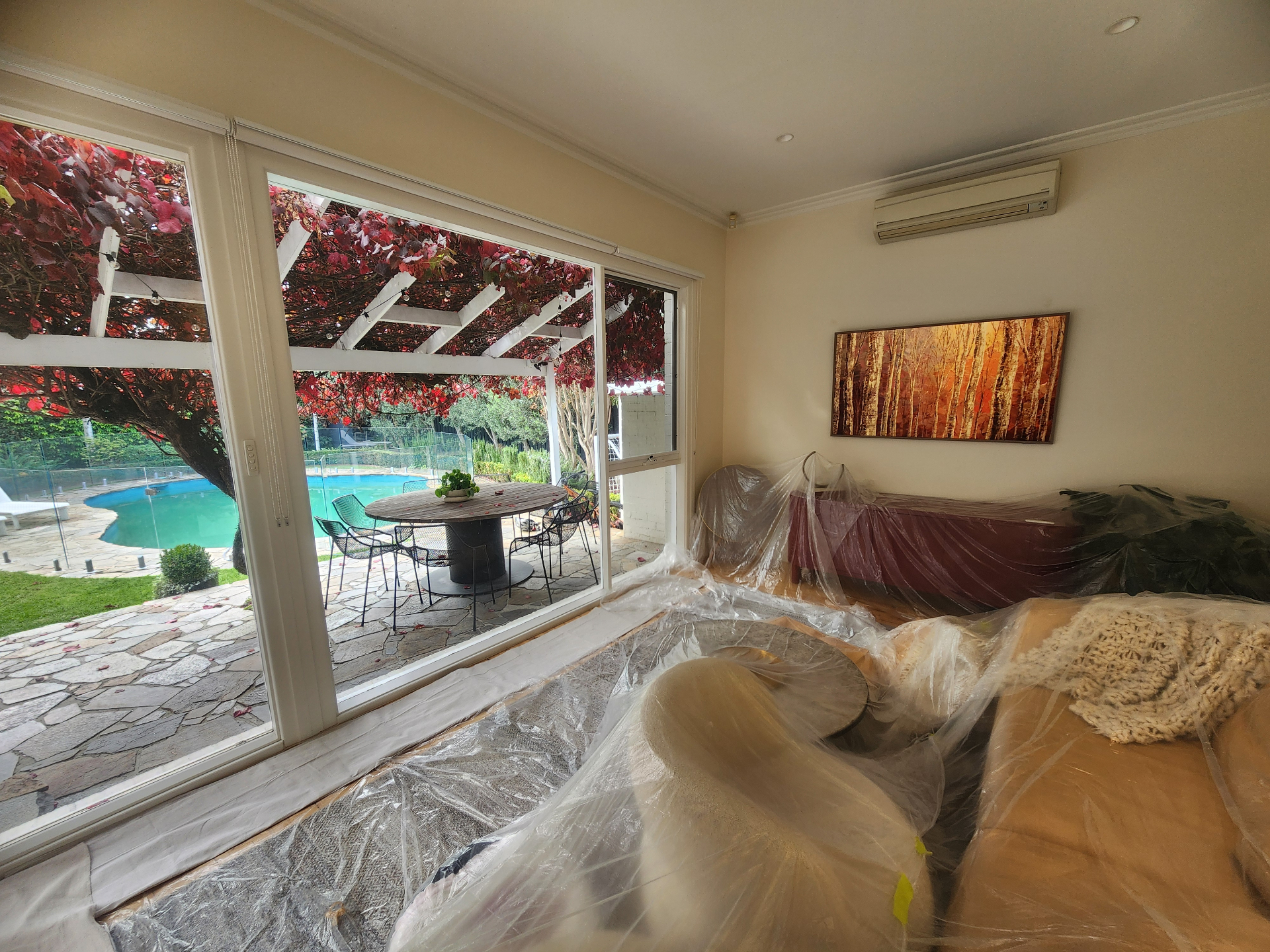 Living room furniture and floors carefully protected with drop sheets before painting, with the garden and pool visible through sliding doors